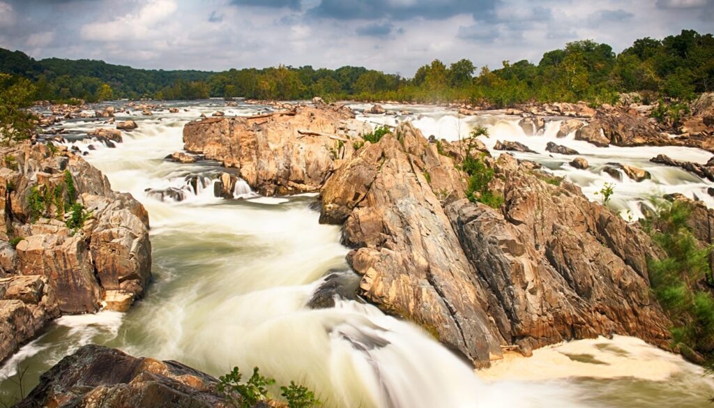 anoramic view of Great Falls with cascading rapids framed by rugged cliffs and lush greenery."